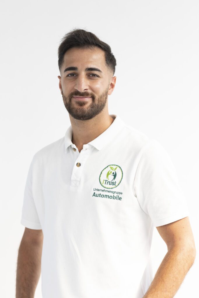 Über uns: Süleyman Tün (Mitarbeiter) posiert für ein Porträtfoto im weißen Poloshirt mit dem Unternehmenslogo.