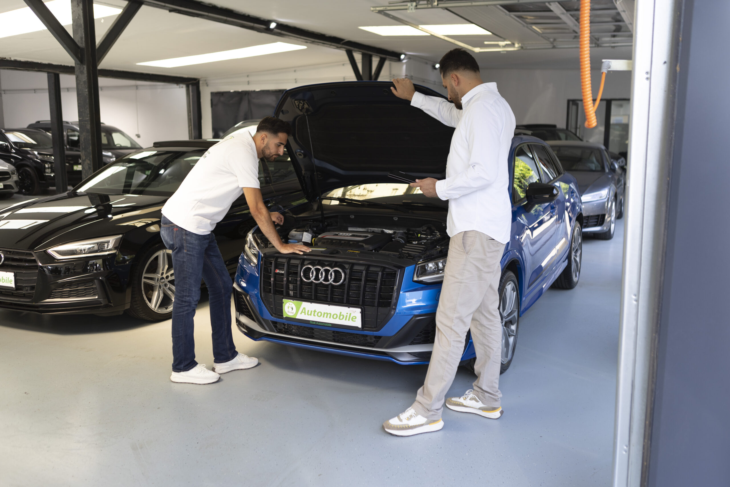 Über iTrust Automobile prüfen Sefkan- und Suleyman Tün den Motorraum eines blauen Audi-Gebrauchtwagens in Solingen.
