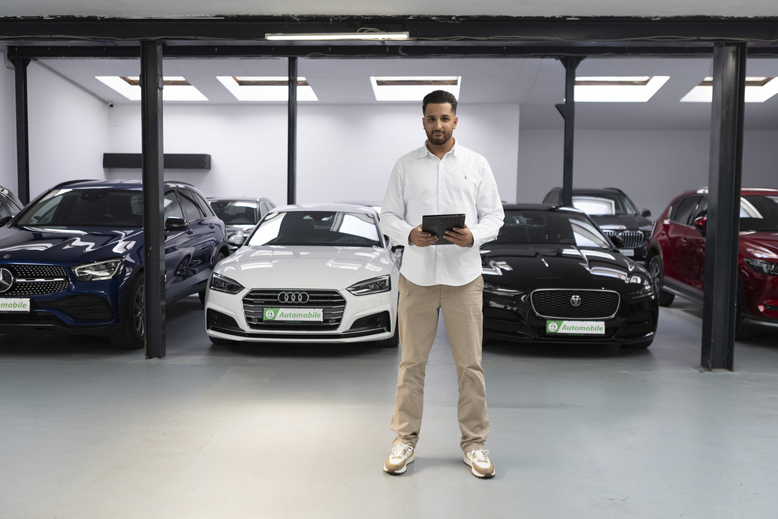 Über iTrust Automobile steht Sefkan Tün mit dem Tablet zwischen einem Audi und Jaguar im Autohaus in Solingen.